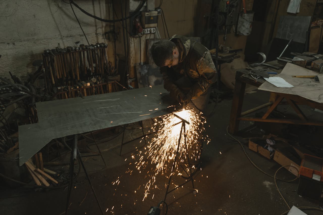 A welder in a workshop creating sparks while working on a metal sheet.